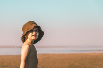 Fototapeta na wymiar Portrait of a little boy 3 years old in a brown panama hat on the beach. Copy space