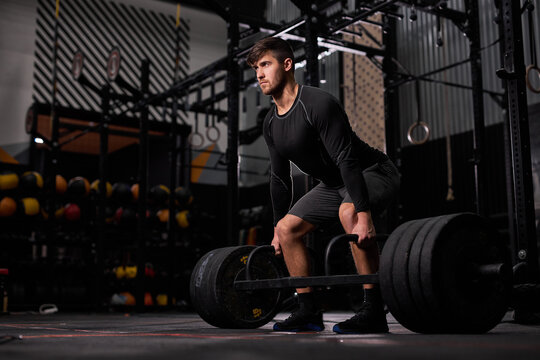 strong fit man training with heavy weights at gym, young caucasian guy in black sportswear do workout exercises alone. fitness, sport concept