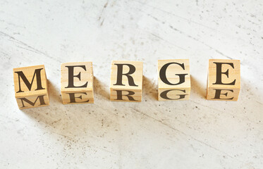 Five wooden cubes with word MERGE on white stone like board, view from above