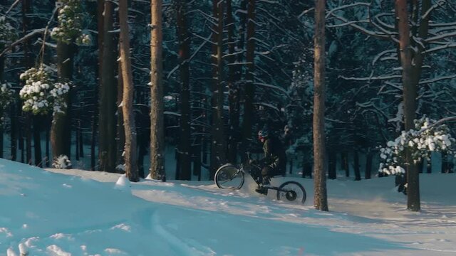 Cyclist in Black Clothes, Helmet and Snow Glasses Riding on Electric Bike in the Snow in Winter Forest. E-Bike Riding and Drifting at Cold Sunny Day - Slow Motion