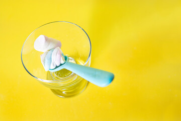 Sweet marshmallows in a glass with a pink spoon, in a yellow background,