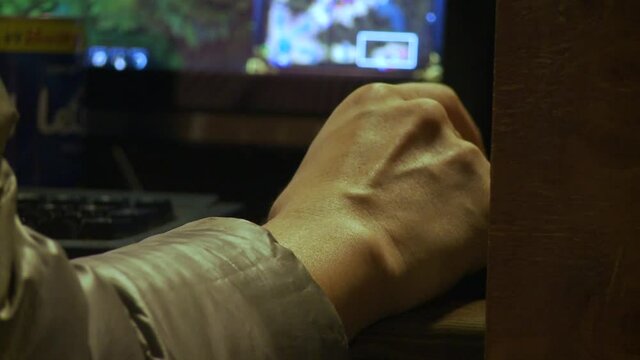 Close up shot of an online gaming addicted's hand clicking frenetically on the mouse i front of a computer screen with confused graphics.