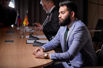 Fototapeta premium arabic male sits listening to colleagues speech , looking at side, wearing elegant formal suit, discussing startups and finance, at interracial business meeting