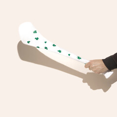A male hand holding white hurling stick, hurley with  with shamrock decoration. Beige background.
