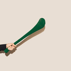 A male hand holding green hurling stick, hurley against beige background.