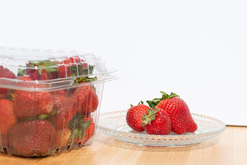 Clear plastic containers of fresh red, ripe strawberries with the stems still on them. The packages are stacked on top of each other on a grocery store shelf.  The berries are firm, rich, and vibrant.