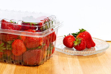 Clear plastic containers of fresh red, ripe strawberries with the stems still on them. The packages are stacked on top of each other on a grocery store shelf.  The berries are firm, rich, and vibrant.