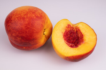 half of the peach lies with the pulp upside down without pits, and next to it is a whole peach