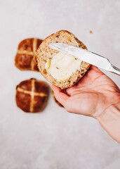 Woman hand holding traditional Easter hot cross bun with butter and knife