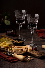 Cheese platter with different cheeses, sliced pear, nuts and honey and glasses of red wine on rustic wooden background. Retro styled cheese variety selection on wood board. Selective focus. High