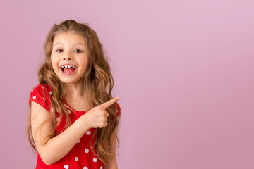 A little girl with curly hair points her finger to the side. Copy space.