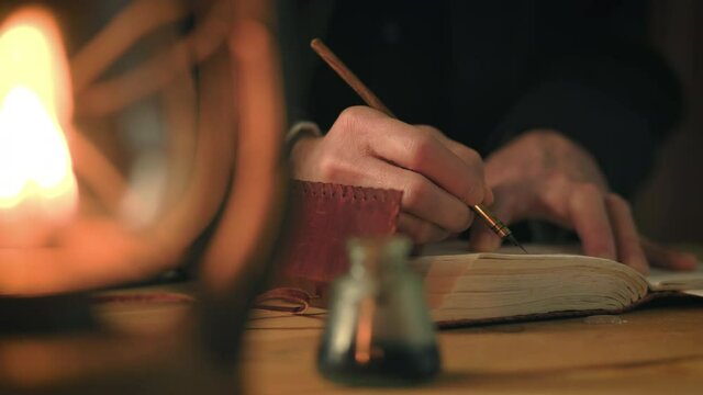 Nineteenth century type scene lit by the light from an oil lamp of a man writing in a journal using a dip pen.