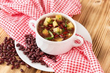 Delicious soup of fresh red beans with the addition of meat, potatoes and herbs on a wooden background.
