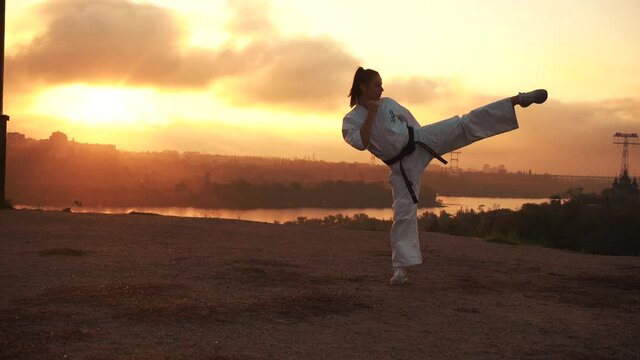 Translation: Kyokushinkai. girl warms up, trains stretching, kick in karate. Harmony with nature. Autumn at sunset. In the background, the golden river, the sun forest, the bridge, the city, the