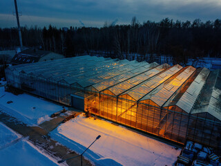 Glowing modern glass greenhouse in winter night, aerial view