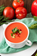 Spanish gazpacho soup on a wooden background with tomatoes and herbs.