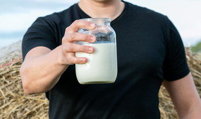 a man holds a jar of fresh milk in his hand on the background of a field with hay