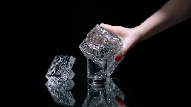 Female hand takes crystal decanter from mirror surface, pours vodka into glass