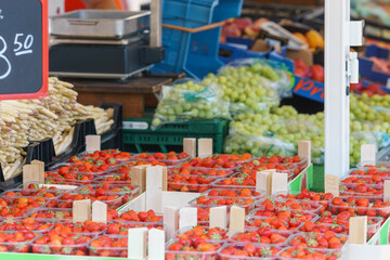 Red strawberries in the plastic tray in wooden boxes and green grapes in the background at market stall