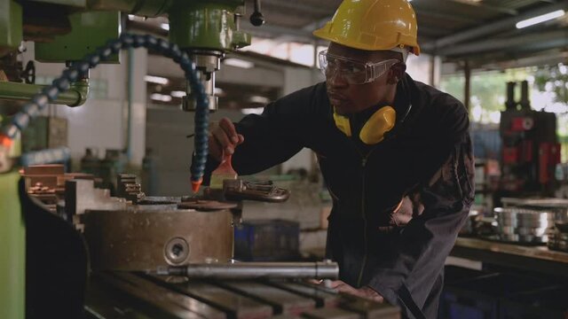 Professional technician african american man in uniform wearing hardhat and goggles with earmuff is standing cleaning and protect rust by oil coating to chucks of milling machine in factory industrial