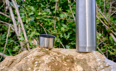 Naklejka premium Caffe mug and heat sealing thermos cover made of stainless steel on thee rock by taking photo during trekking in wild nature in forest