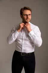A man in a white shirt, dark trousers, black boots and glasses stands against a plain background, looking away. Business clothes. Confident look. Success