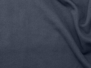 The texture detail of a dark blue, polyester, mesh baseball jersey is shown in a closeup view with room for copyspace / text space to the left.
