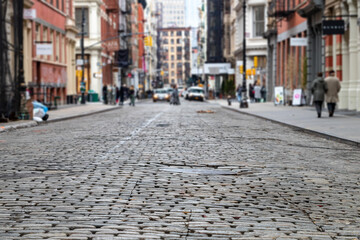 Cobblestone street with busy intersection blurred in the background in the SoHo neighborhood of New...