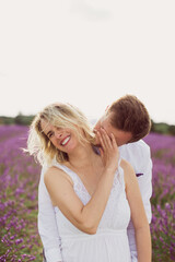 Fototapeta premium The young man kissing his smiling pregnant wife in the lavender field