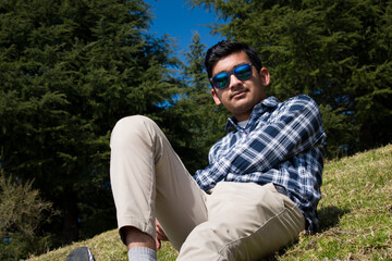 indian boy laying down on green grass field and posing for picture wearing blue sunglasses
