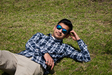 boy laying down on green grass field and looking into camera wearing blue sunglasses