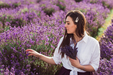 Portrait of the charming young brunette who is gathering flowers in the lavender field