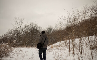 Man walking through snow covered forest. Cold winter day in Ontario Canada. Bare brown trees surround forest