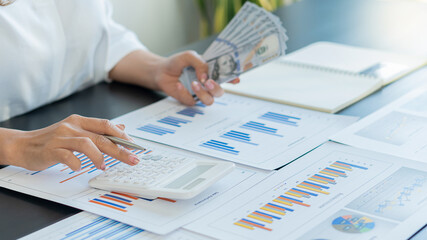 Young woman holding a pen and pressing a calculator, and her left hand holds money, plans, summarizes and calculates the finances in the office.