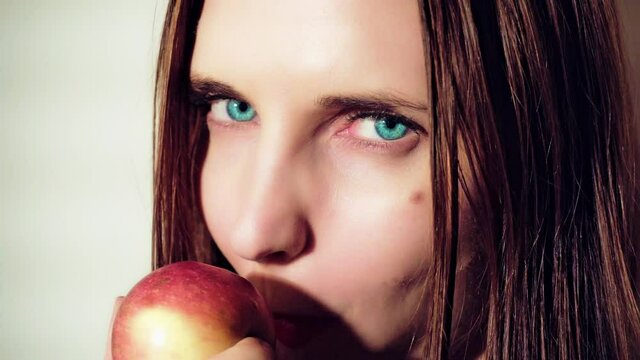 Woman eating apple. Woman seduces eating apple. Close up portrait of a young girl biting and eating red apple and looking at the camera. Apple Temptation.
