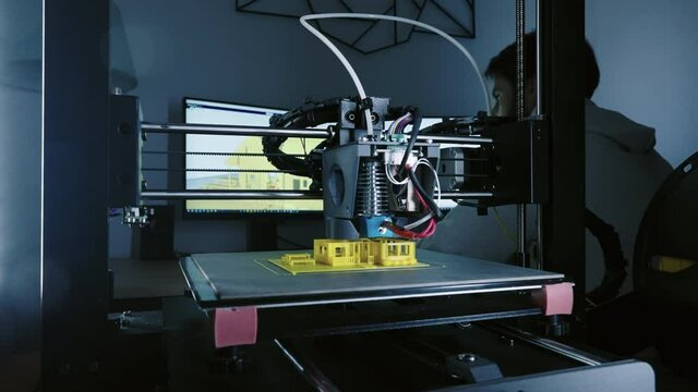 3d Printer printing yellow small house with engineer constructor in background at pc model shot in 4k