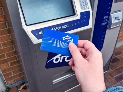 Bellevue, WA / USA - circa December 2019:  Person's hand holding a bright blue ORCA transit pass in front of an ORCA card vending and refill machine at Bellevue Transit Center downtown.
