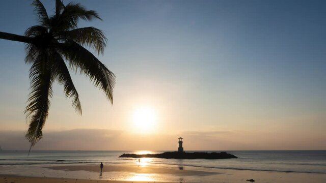 sunset at the beach, silhouette palm tree and a small lighthouse at golden sandy beach. calm sea water in low tithe people enjoining colorful sunlight and soft clear blue sky. timelapse footage nature