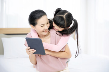 Happy loving asian family. Mother and her daughter child girl playing and hugging on bed in bedroom