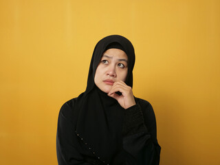 Asian muslim woman wearing hijab shows thinking contemplating expression. Looking for solution of a problem. Against yellow background