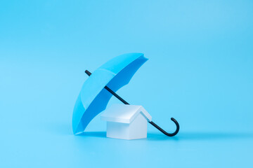 Renters home insurance or mortgage protection concept with a 3D house model under a blue umbrella © Kenishirotie