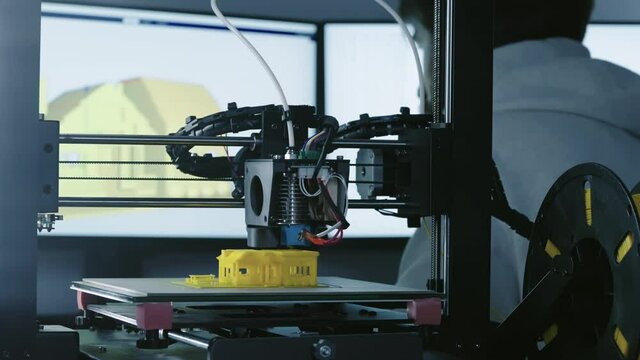 3d Printer printing yellow small house with engineer constructor in background at pc model shot in 4k