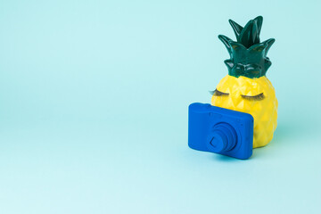 Fototapeta premium A yellow pineapple with a blue camera takes pictures of a pumpkin in a hat.