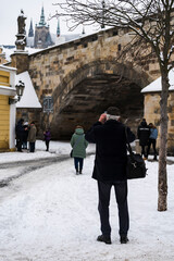 view of a silhouette of a photographer photographing a snow covered tower on Charles Bridge in winter 2021 during the day