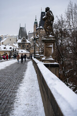 Fototapeta premium view of snow-covered statues and street lights on old stones Charles Bridge on the Vltava River in winter in the center of the town and on the bridge 