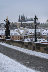 Fototapeta na wymiar view of snow-covered statues and street lights on the old stones of Charles Bridge on the Vltava River and in the background the snow-covered Prague Castle 
