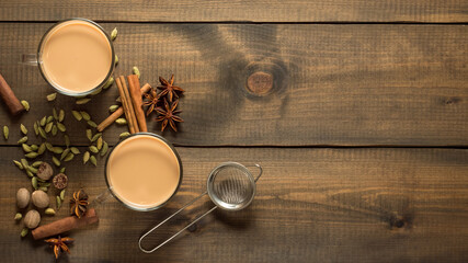 Two mugs with masala tea stand on a wooden table with spices. Top view. Copy space.