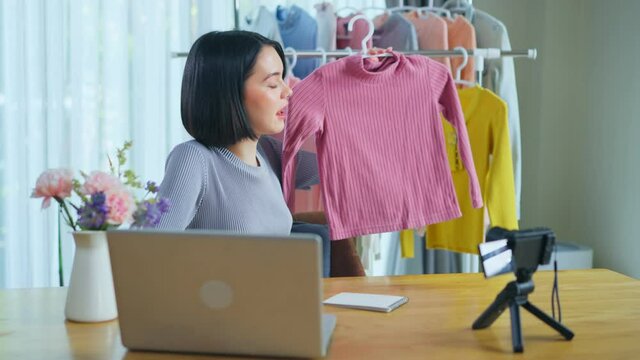 Asian young beautiful girl selling clothes online by live streaming.
