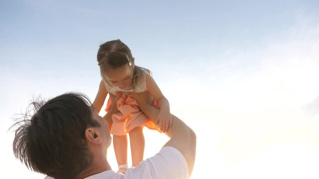 Dad raised his healthy happy daughter in his arms to blue sky. Dad and little child play together outdoors. Family games. Baby and daddy in the park. Daddy's day off. Happy family and childhood
