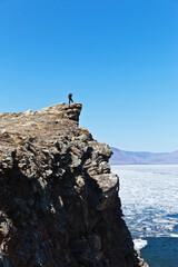 Baikal Lake in sunny May day. A tourist photographs an ice drift in the Small Sea Strait from a high cliff. Spring travel and active holidays